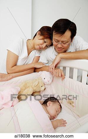 Mother and father looking at baby sleeping in crib View Large Photo Image Stock Photo - Mother and father looking at baby sleeping in crib. Fotosearch