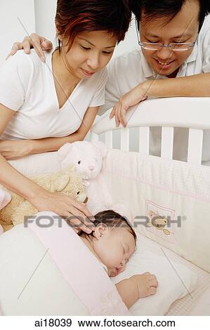 Stock Photo - Mother and father looking at sleeping baby. Fotosearch