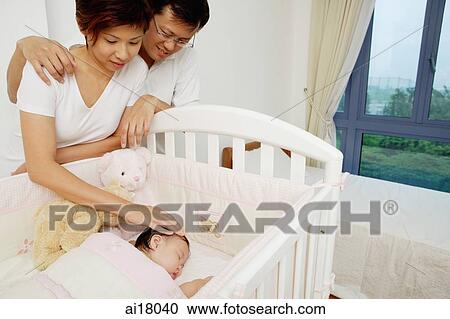 Mother and father standing next to crib looking at sleeping baby View Large Photo Image Stock Image - Mother and father standing next to crib looking at sleeping baby. Fotosearch