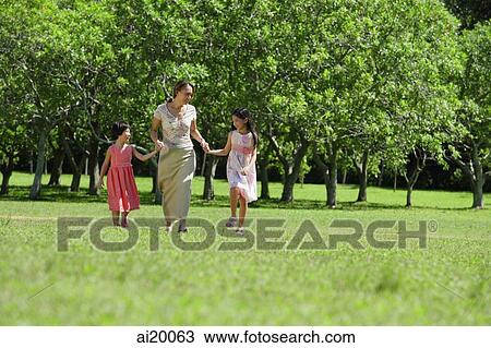 Stock Image - Mother and two daughters holding hands, walking across park. Fotosearch