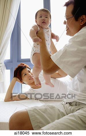Stock Photography - Mother lying on bed, father carrying baby girl. Fotosearch