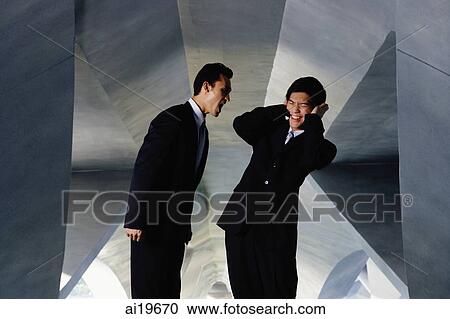 Stock Image - One businessman shouting, the other businessman covering his ears. Fotosearch