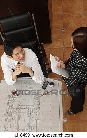 Stock Photo - Seated businessman smiling at executive standing next to him. Fotosearch