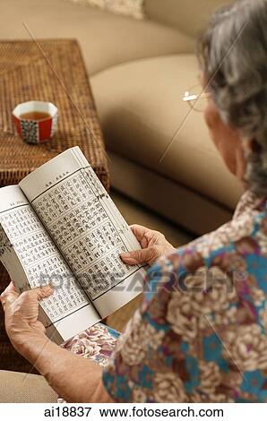 Stock Photo - Senior woman at home, reading a book, over the shoulder view. Fotosearch