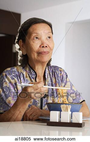 Stock Photography - Senior woman having noodles at home, looking away. Fotosearch