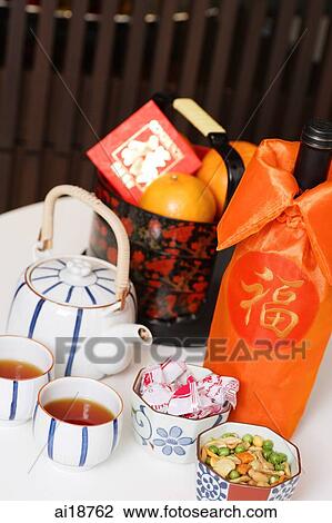 Stock Image - Still life with basket of oranges, red packet, teapot, teacups and bottle of wine. Fotosearch