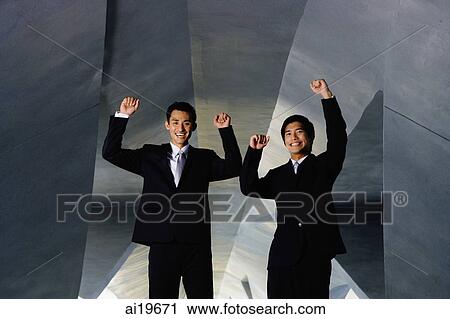 Stock Image - Two businessmen looking at camera, hands raised in the air. Fotosearch
