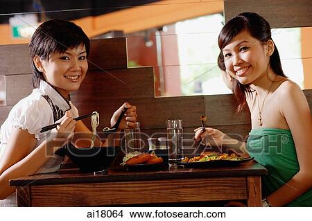 Two young women sitting at table in restaurant, smiling at camera View Large Photo Image Picture - Two young women sitting at table in restaurant, smiling at camera. Fotosearch