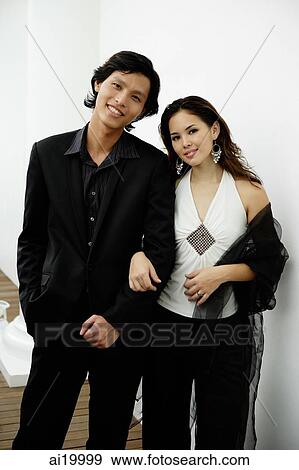 Stock Photo - Well dressed couple standing arm in arm, looking at camera. Fotosearch