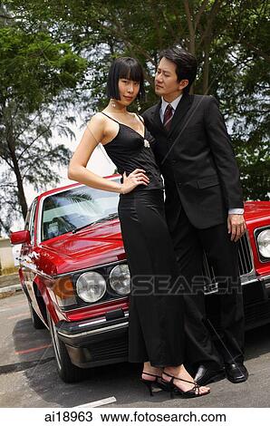 Well dressed couple standing in front of red car View Large Photo Image Stock Image - Well dressed couple standing in front of red car. Fotosearch