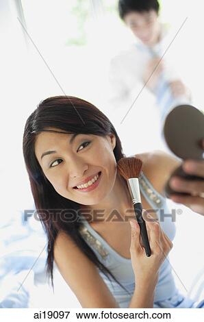 Stock Photo - Woman applying make-up, looking at compact. Fotosearch
