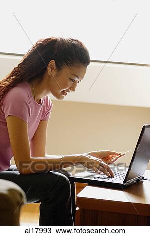 Stock Image - Woman at home, holding credit card and using laptop. Fotosearch