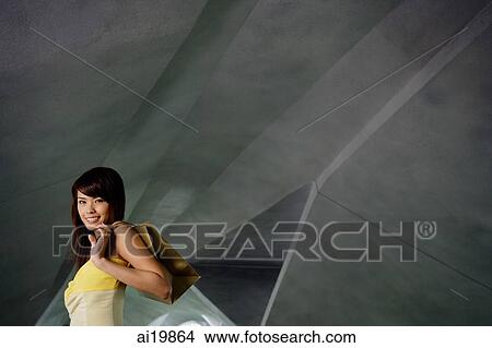 Woman carrying shopping bag over shoulder, looking at camera View Large Photo Image Picture - Woman carrying shopping bag over shoulder, looking at camera. Fotosearch