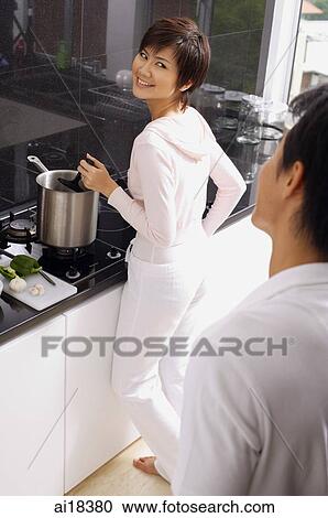 Stock Image - Woman cooking on stove, looking over shoulder at man standing behind her. Fotosearch