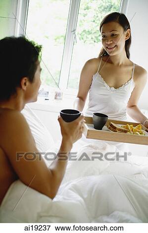 Woman holding breakfast tray, man sitting in bed holding cup View Large Photo Image Stock Photo - Woman holding breakfast tray, man sitting in bed holding cup. Fotosearch