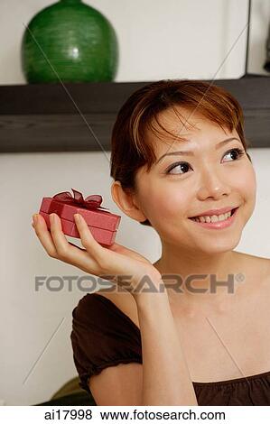 Woman holding gift box to ear View Large Photo Image Stock Photo - Woman holding gift box to ear. Fotosearch