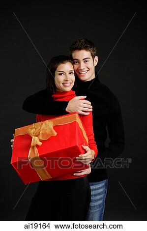 Woman holding gift, man embracing her View Large Photo Image Picture - Woman holding gift, man embracing her. Fotosearch