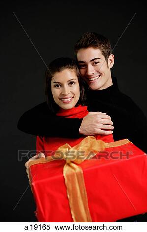 Stock Photography - Woman holding red gift, man embracing her. Fotosearch