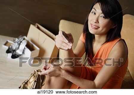 Stock Image - Woman holding shoes and credit card, looking at camera, smiling. Fotosearch
