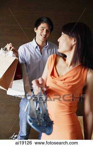 Stock Photograph - Woman holding shoes, looking over shoulder at man carrying shopping bags. Fotosearch