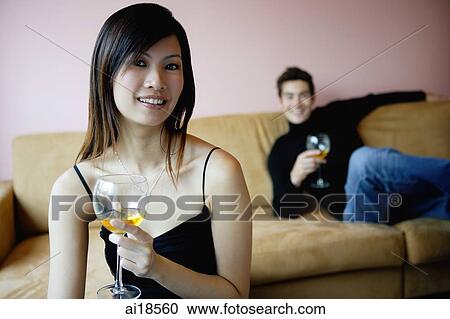 Stock Image - Woman holding wine glass, smiling at camera, man in the background. Fotosearch