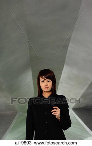 Stock Image - Woman in black jacket, holding phone, looking at camera. Fotosearch