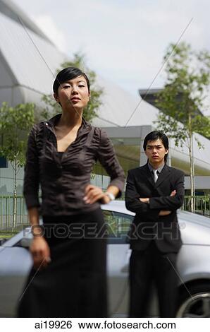 Woman in foreground, with hand on hip, man in background, leaning on car View Large Photo Image Stock Photograph - Woman in foreground, with hand on hip, man in background, leaning on car. Fotosearch