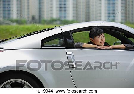 Woman in front seat of silver sports car, looking out the window, smiling View Large Photo Image Picture - Woman in front seat of silver sports car, looking out the window, smiling. Fotosearch