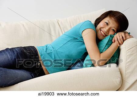 Stock Image - Woman in turquoise top lying on sofa, looking at camera. Fotosearch