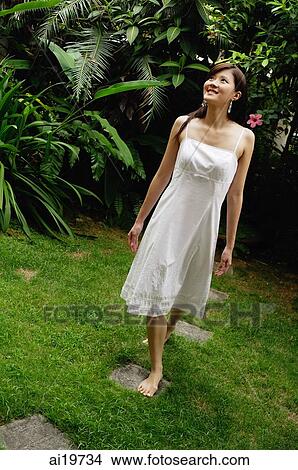 Picture - Woman in white dress, barefoot in garden. Fotosearch