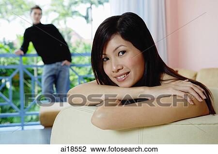 Woman leaning head on folded arms, looking at camera, man in the background View Large Photo Image Stock Image - Woman leaning head on folded arms, looking at camera, man in the background. Fotosearch