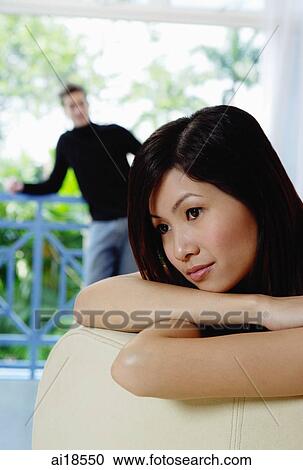 Woman leaning on back of sofa, looking away, man in the background View Large Photo Image Stock Image - Woman leaning on back of sofa, looking away, man in the background. Fotosearch