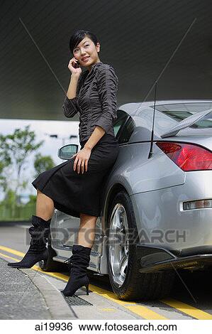 Woman leaning on car, using mobile phone View Large Photo Image Stock Photograph - Woman leaning on car, using mobile phone. Fotosearch
