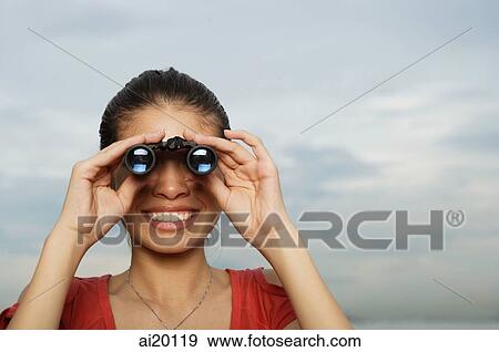 Stock Photo - Woman looking through binoculars, head shot. Fotosearch