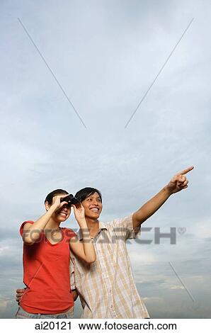 Woman looking through binoculars, man next to her pointing in the distance View Large Photo Image Stock Image - Woman looking through binoculars, man next to her pointing in the distance. Fotosearch