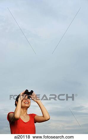 Stock Photo - Woman looking through binoculars, smiling. Fotosearch