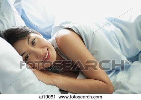 Stock Image - Woman lying in bed, smiling at camera. Fotosearch