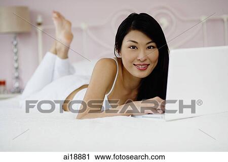 Woman lying on bed, using laptop, smiling at camera View Large Photo Image Stock Image - Woman lying on bed, using laptop, smiling at camera. Fotosearch