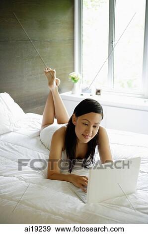 Woman lying on bed, using laptop View Large Photo Image Stock Photo - Woman lying on bed, using laptop. Fotosearch