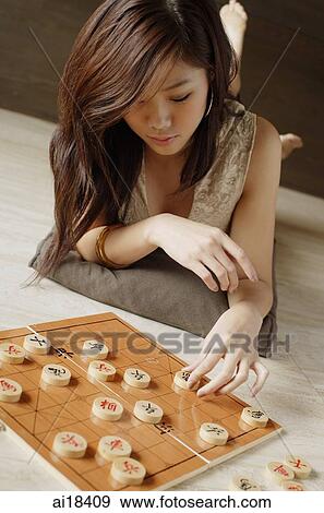 Stock Photo - Woman lying on floor, playing with Chinese chess board. Fotosearch