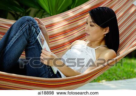 Stock Photo - Woman lying on hammock, reading magazine. Fotosearch