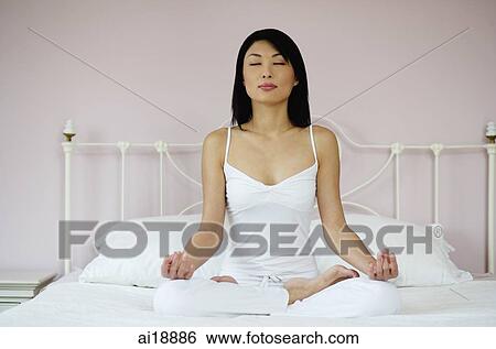 Stock Photograph - Woman on bed, sitting in lotus position. Fotosearch
