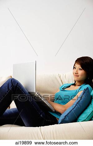 Stock Photo - Woman on sofa, using laptop. Fotosearch