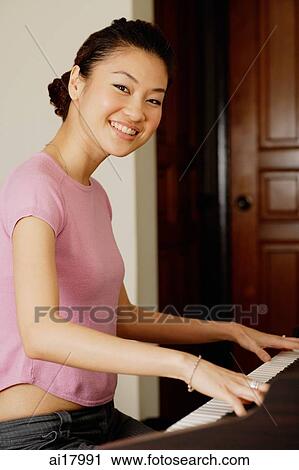 Stock Image - Woman playing piano, smiling at camera. Fotosearch