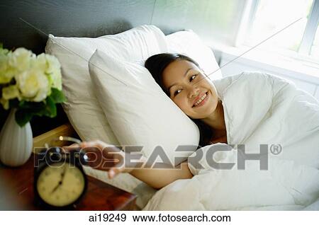 Woman reaching for alarm clock on bedside table View Large Photo Image Stock Photo - Woman reaching for alarm clock on bedside table. Fotosearch