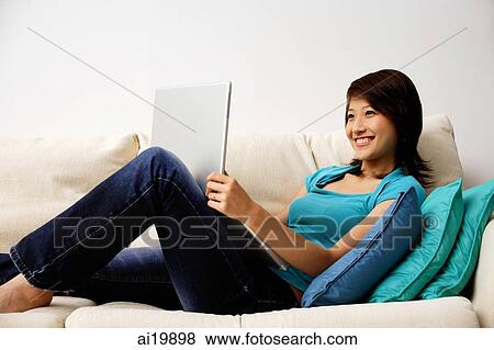 Woman reclining on sofa, using laptop View Large Photo Image Stock Photo - Woman reclining on sofa, using laptop. Fotosearch