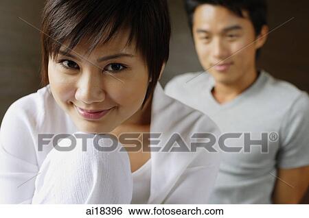 Woman resting chin on knee, smiling at camera, man in the background View Large Photo Image Stock Photograph - Woman resting chin on knee, smiling at camera, man in the background. Fotosearch