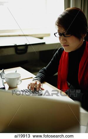 Stock Image - Woman sitting at desk with calculator and laptop. Fotosearch