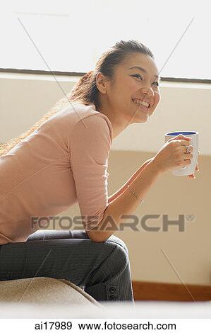 Woman sitting at home, holding mug View Large Photo Image Stock Photo - Woman sitting at home, holding mug. Fotosearch