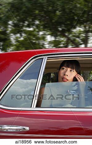 Stock Photograph - Woman sitting in car, using mobile phone, looking through the window. Fotosearch